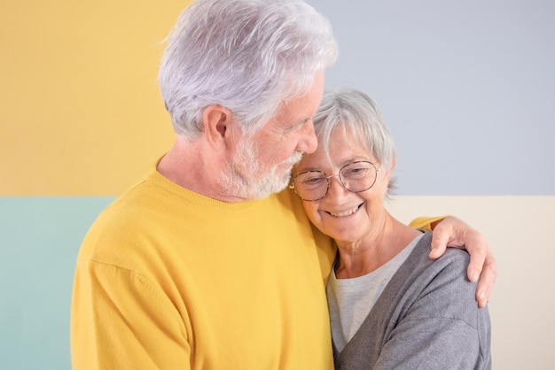 Encantadora y atractiva pareja mayor caucásica abrazándose sobre un fondo colorido aislado Anciano de pelo blanco mirando a su esposa sonriendo disfrutando de buena compañía y tiempo libre