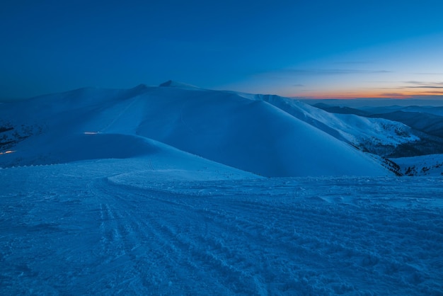 Encantadora bela vista das montanhas e colinas no vale nevado no final da noite. Conceito de beleza do campo de inverno e relaxamento de fim de semana de inverno. Copyspace