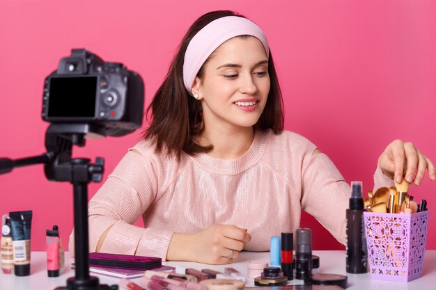 La encantadora bloguera muestra productos cosméticos mientras graba videos y da consejos para su blog de belleza, mira hacia otro lado cámara digital