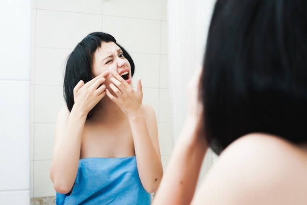 Encantadora chica de cabello oscuro después de una ducha aprieta un grano en su cara