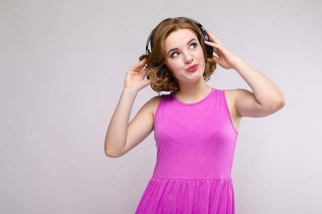 Encantadora chica joven en vestido rosa sobre fondo gris. Niña con auriculares sonriendo