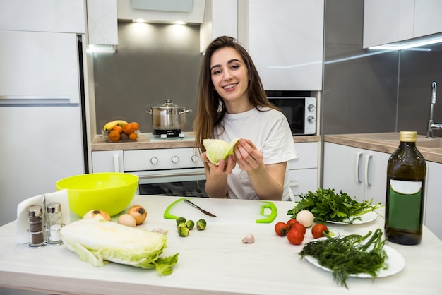 Encantadora chica prepara una ensalada de diferentes verduras y verduras aromatizadas con aceite de oliva para un estilo de vida saludable