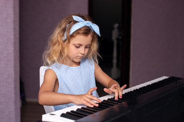 una encantadora chica rubia con un vestido azul toca el piano en su dormitorio