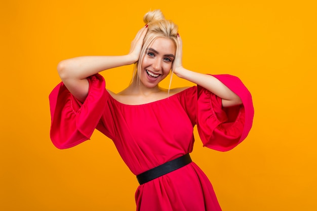 Encantadora chica rubia con un vestido rojo sobre un fondo amarillo de estudio