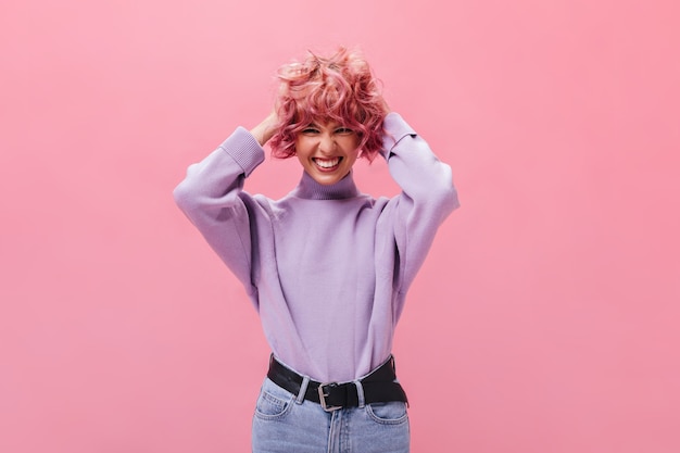 Encantadora chica en suéter morado con volantes de pelo corto rizado rosa