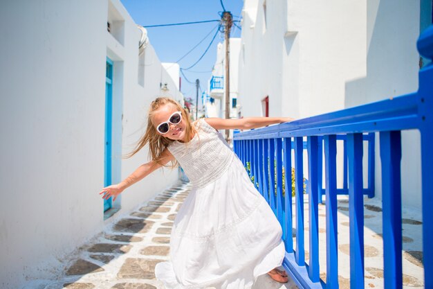 Encantadora chica en vestido blanco al aire libre en las viejas calles de Mykonos. Cabrito en la calle del típico pueblo tradicional griego con paredes blancas y coloridas puertas en la isla de Mykonos, en Grecia