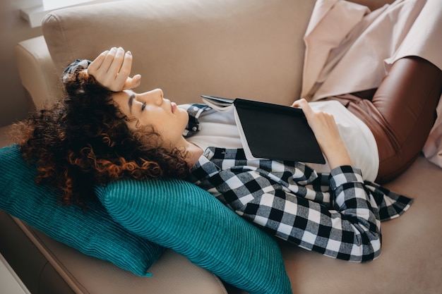 Encantadora dama caucásica acostada en la cama con almohadas azules cerrando los ojos después de leer un libro