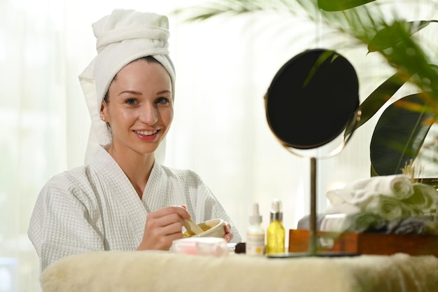 Encantadora dama caucásica preparando yogur y cúrcuma para máscara facial Tratamiento de belleza y concepto de autocuidado