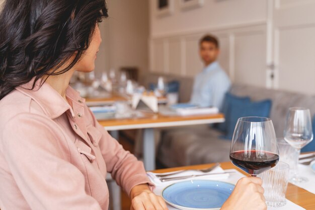 Encantadora dama morena sosteniendo una copa de vino y mirando al caballero en la cafetería