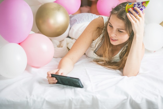 Encantadora dama en pijama haciendo selfie en su habitación usando el teléfono. Feliz cumpleaños.