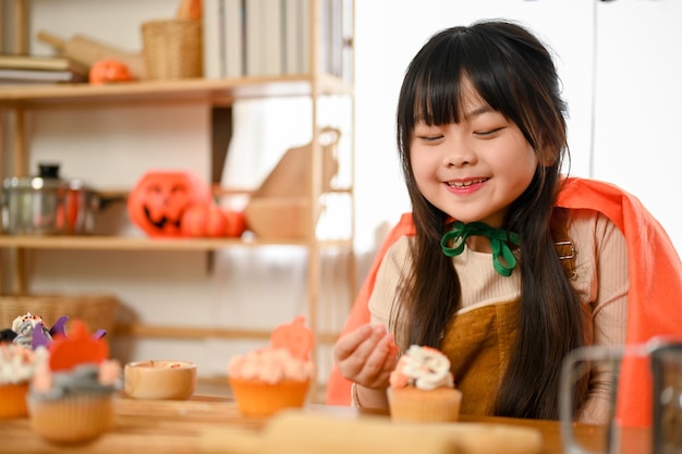 Encantadora e adorável garotinha asiática em traje de halloween gosta de fazer cupcake de Halloween