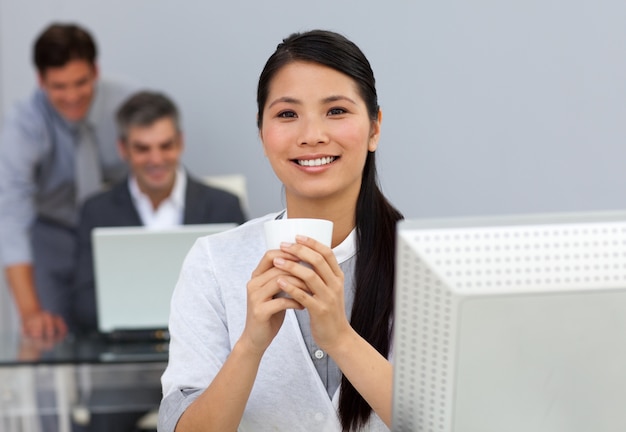 Encantadora empresaria asiática bebiendo un café en su escritorio
