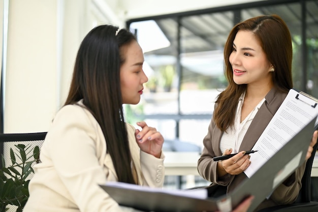 Encantadora empresária asiática mostrando um novo relatório de negócios para seu colega