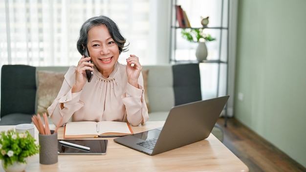Encantadora empresária asiática sênior falando ao telefone com seu fornecedor de negócios