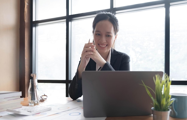 Encantadora empresária asiática sentada trabalhando no laptop no escritório