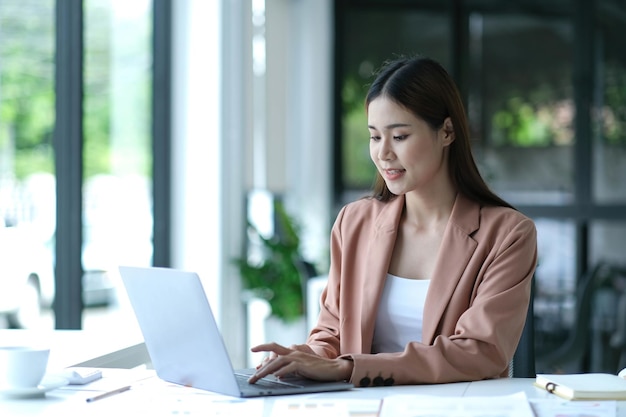 Encantadora empresária asiática sentada trabalhando no laptop no escritório