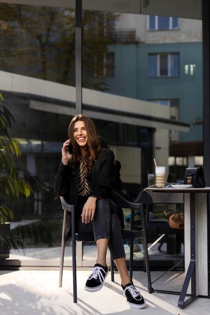 Encantadora empresária sorridente está falando em um telefone celular sentado em um café Um copo com uma bebida de café está sobre a mesa