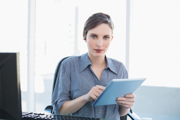 Encantadora empresaria usando su tableta sentado en su escritorio