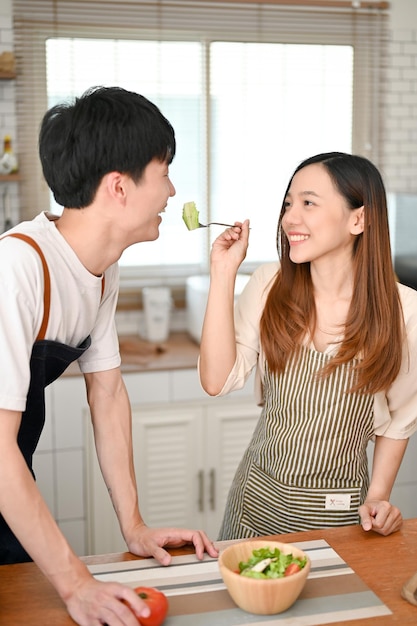 Encantadora ensalada asiática alimentando a su novio en la cocina disfruta haciendo el almuerzo juntos