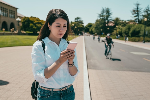 encantadora estudante internacional asiática procurando em um telefone seu destino enquanto atravessa a estrada.