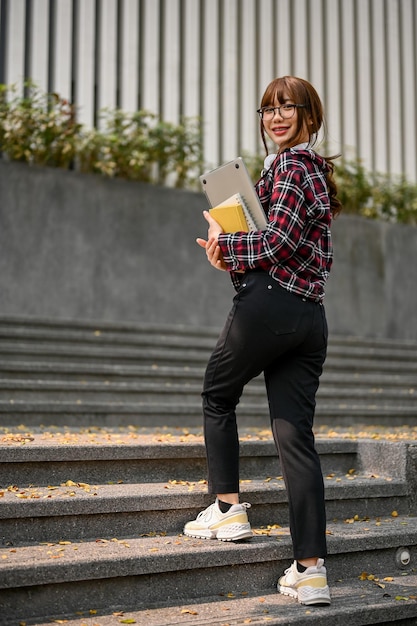 Encantadora estudiante universitaria asiática subiendo las escaleras fuera del edificio del campus