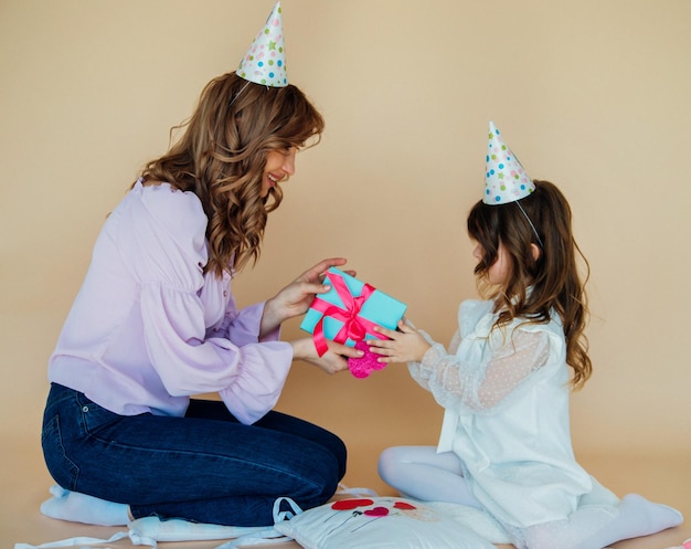 Encantadora família alegre sentada no chão e se divertindo durante o tempo festivo conceito de aniversário mãe e filha se felicitam