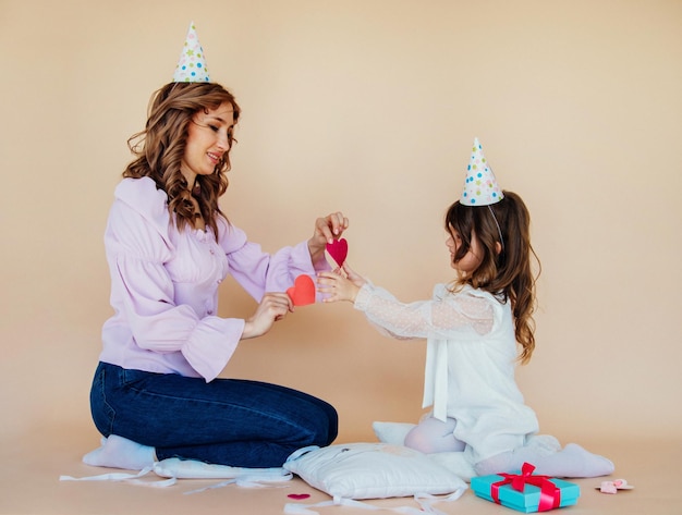 Encantadora familia alegre sentada en el suelo y divirtiéndose durante el tiempo festivo Concepto de cumpleaños Mamá e hija se felicitan mutuamente