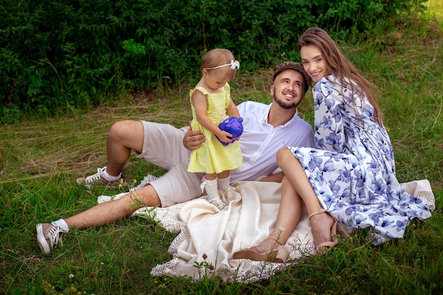 Encantadora familia divirtiéndose en el parque. Padres con hija relajándose al aire libre.