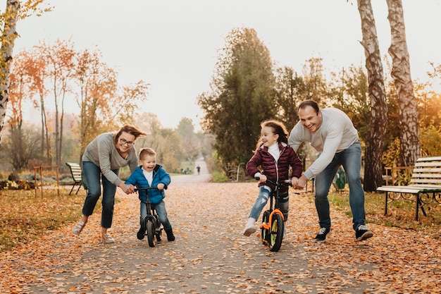 Encantadora familia jugando con sus hijos mientras les enseña a andar en bicicleta en el parque.