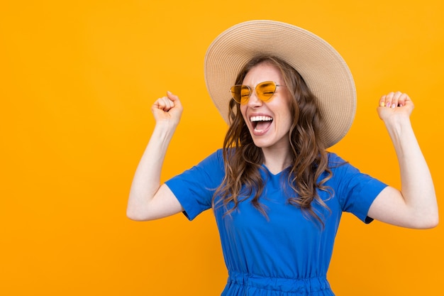 Encantadora feliz glamorosa hermosa joven en un sombrero de paja y gafas en una pared naranja