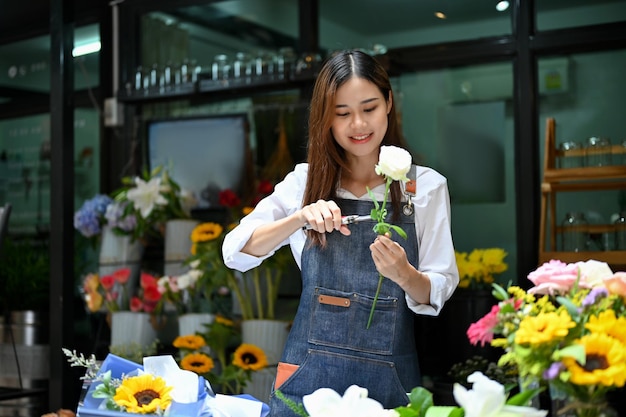 Encantadora florista asiática o dueña de una tienda de flores haciendo un hermoso ramo de rosas