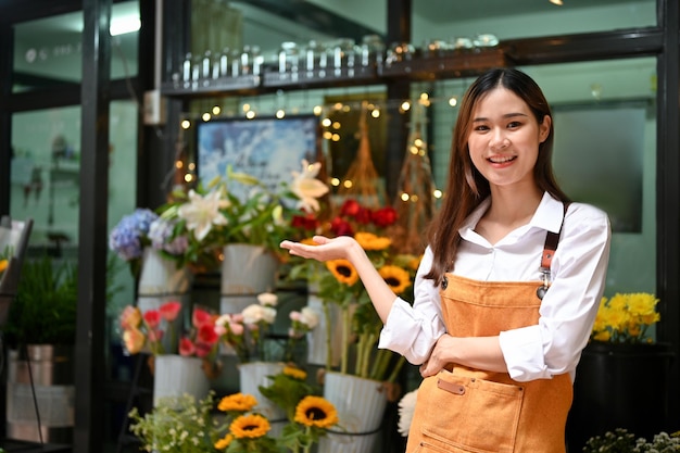 Encantadora florista asiática ou dona de floricultura fica na frente de sua floricultura