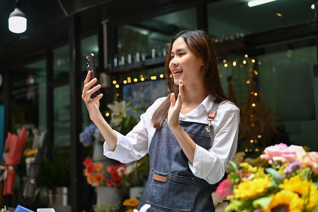 Encantadora florista asiática usando un teléfono inteligente transmitiendo en vivo en las redes sociales de su floristería