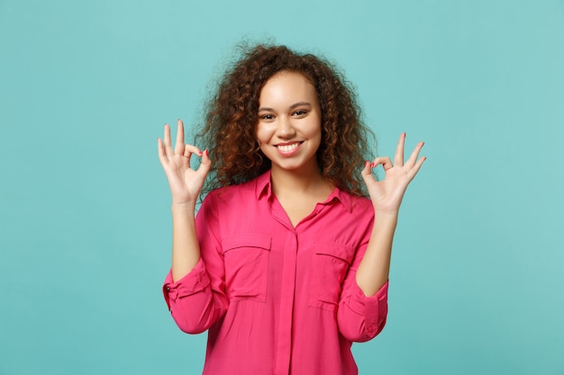 Foto encantadora garota afro-americana com roupas casuais, mostrando o gesto ok, olhando a câmera isolada no fundo da parede azul turquesa no estúdio. emoções sinceras de pessoas, conceito de estilo de vida. simule o espaço da cópia.