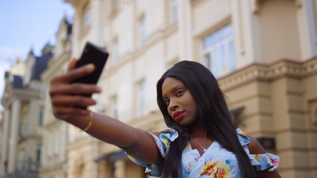 Encantadora garota afro posando na câmera do telefone na rua Senhora segurando celular na cidade