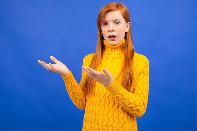 Encantadora garota ruiva Europeia em um suéter amarelo, agitando os braços e indignada em azul