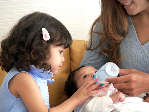 Foto encantadora hermana quédate cerca viendo a mamá alimentar a su hermanito en casa