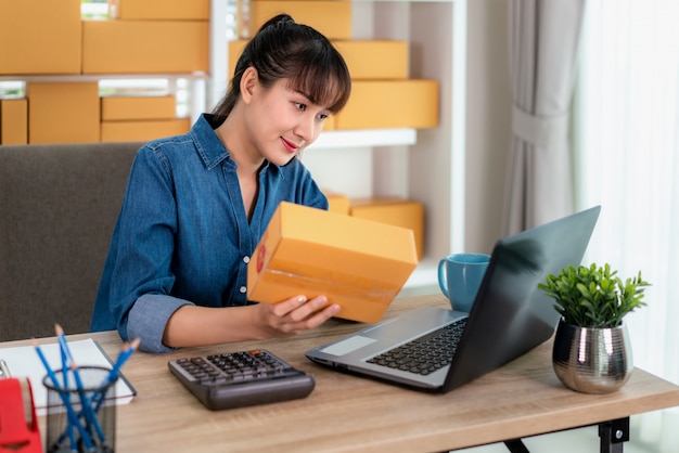 Encantadora hermosa mujer de negocios asiática propietaria adolescente trabaja en casa para ir de compras en línea, verificando los detalles en el buzón con una computadora portátil con equipo de oficina, concepto de estilo de vida empresarial