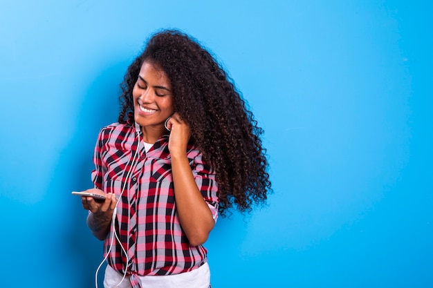 Encantadora incrível jovem afro-americana, dançando enquanto ouve música em fones de ouvido em seu telefone celular.