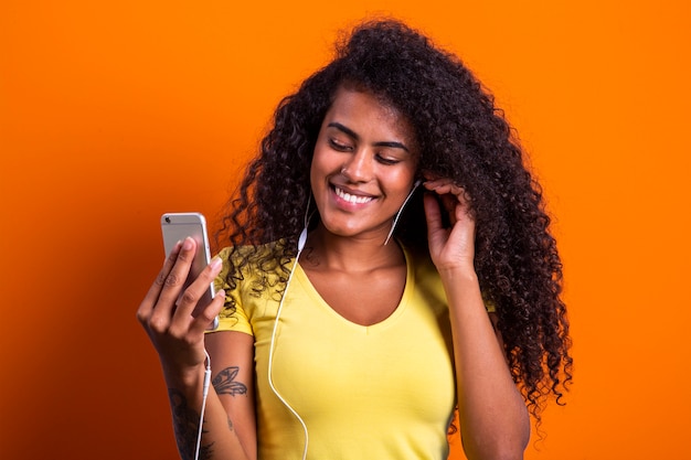 Encantadora incrível jovem afro-americana, dançando enquanto ouve música em fones de ouvido em seu telefone celular.