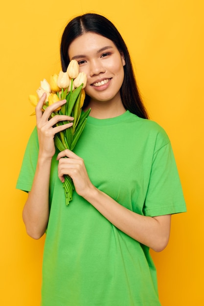 Encantadora jovem asiática camiseta verde um buquê de flores amarelas isoladas de fundo inalterado