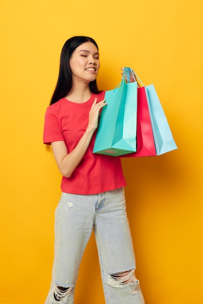 Encantadora jovem asiática com sacos de compras multicoloridos fundo amarelo inalterado