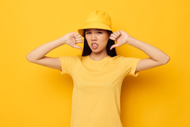 Encantadora jovem asiática em uma camiseta amarela e chapéu posando emoções fundo amarelo inalterado