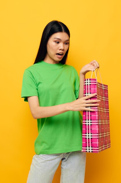 Encantadora jovem asiática pacote de compras de entretenimento fundo amarelo inalterado