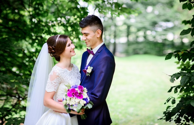 Encantadora jovem casal de noivos admira-se em pé sob o arco de folhas verdes