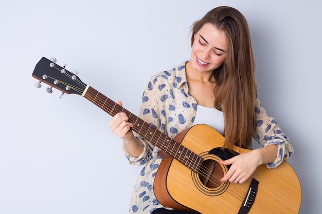 Encantadora jovem de blusa bege tocando guitarra em fundo cinza em estúdio