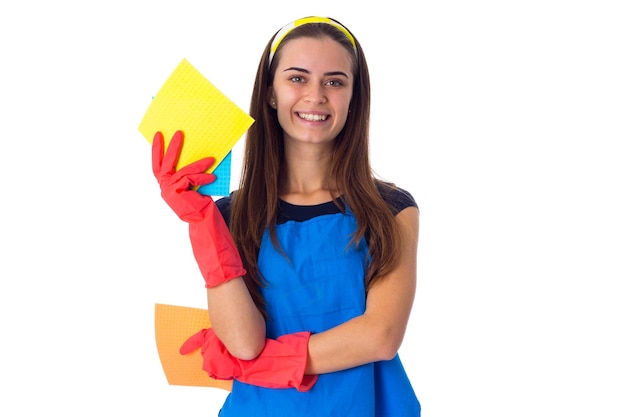 Encantadora jovem de camiseta azul e avental com luvas vermelhas segurando espanadores em fundo branco no estúdio