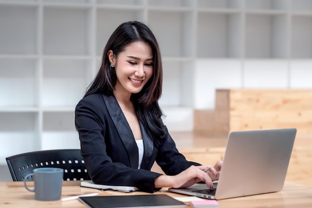 Encantadora jovem empresária asiática trabalhando no teclado do laptop no escritório.