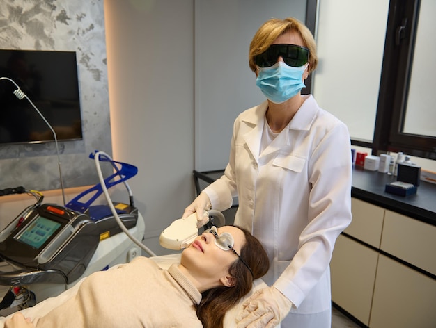 Encantadora jovem europeia recebendo tratamento a laser facial por esteticista na clínica de spa de bem-estar