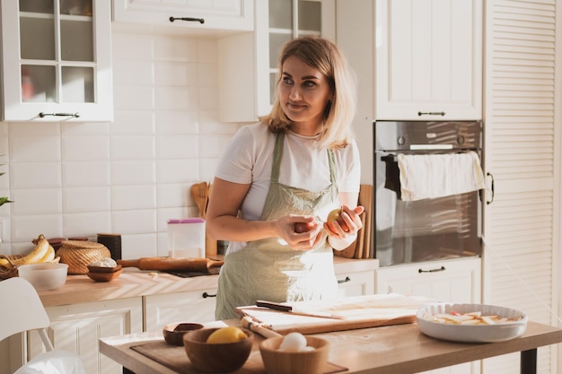 Encantadora jovem no avental do chef preparando torta em casa na cozinha Aconchegante interior de casa